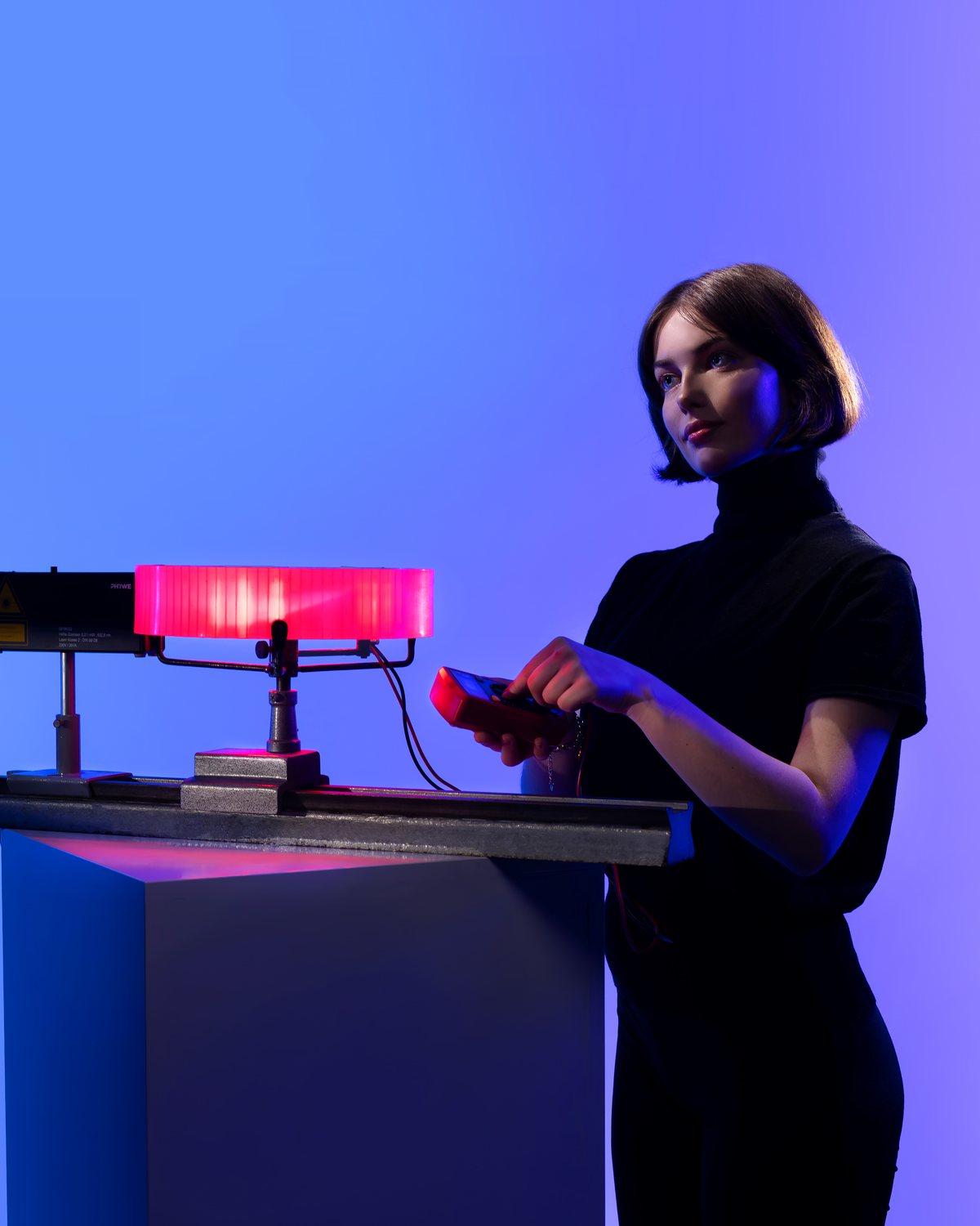 Sofiia Yanovska standing at a table with a glowing red lamp against a blue and violet backdrop